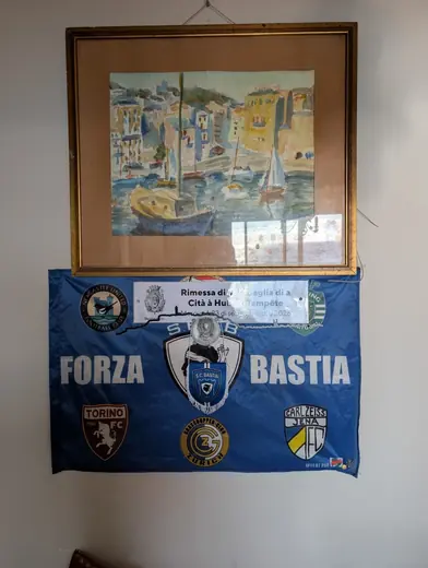 Chez lui : une aquarelle de port au-dessus d’un drapeau « Forza Bastia »