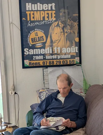 Chez lui, dans son fauteuil, sous l’affiche d’un spectacle au Relais